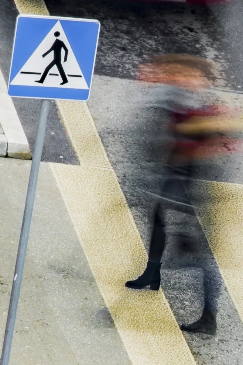 Pedestrian crossing sign beside a blurred red-haired figure on a zebra crossing